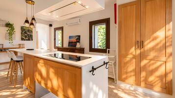 A modern kitchen with a central island, wooden cabinets, pendant lighting, and a view of greenery outside.