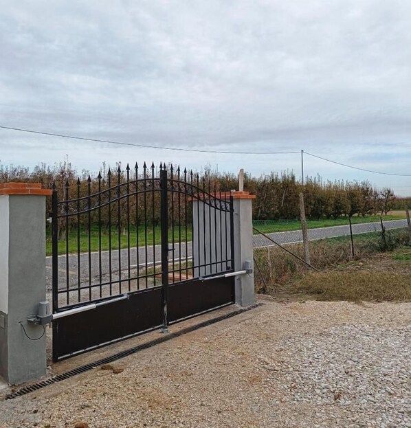 A gated entrance with a metal gate, concrete pillars, and a gravel driveway. - Casa LaSer (Cotignola)