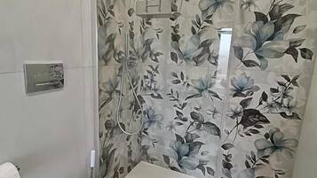 Un bagno con il water, una doccia rivestita di carta da parati floreale e un lavandino bianco.