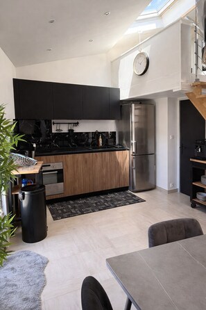 Eine moderne Küche mit schwarzen Schränken, einem Edelstahlkühlschrank und einem Essbereich mit Tisch und Stühlen.