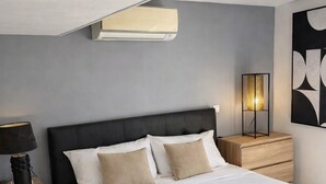 Une chambre moderne avec un grand lit, une lampe de chevet, un climatiseur fixé au mur et une lampe sur pied.
