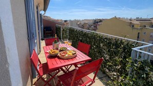 Un balcon avec une table dressée pour deux personnes, une bouteille et un panier rempli de victuailles.
