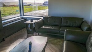 A modern living room with a leather sofa, a small table, and a window offering a view of a rural landscape.