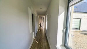 A narrow hallway with a wooden floor, a spiral staircase, and a large window on the right.