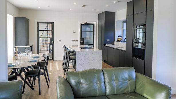 A modern kitchen with dark cabinetry, a central island, and a dining area with a round table and chairs.