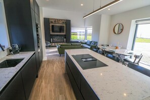 A modern kitchen with a central island, a dining area with a round table, and a living space with a sofa and TV.