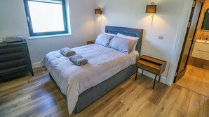 A bedroom with a bed, bedside tables, a window, and a bathroom visible through an open door.
