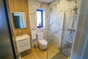 A bathroom with a glass-enclosed shower, a toilet, a sink, and a window with a plant.