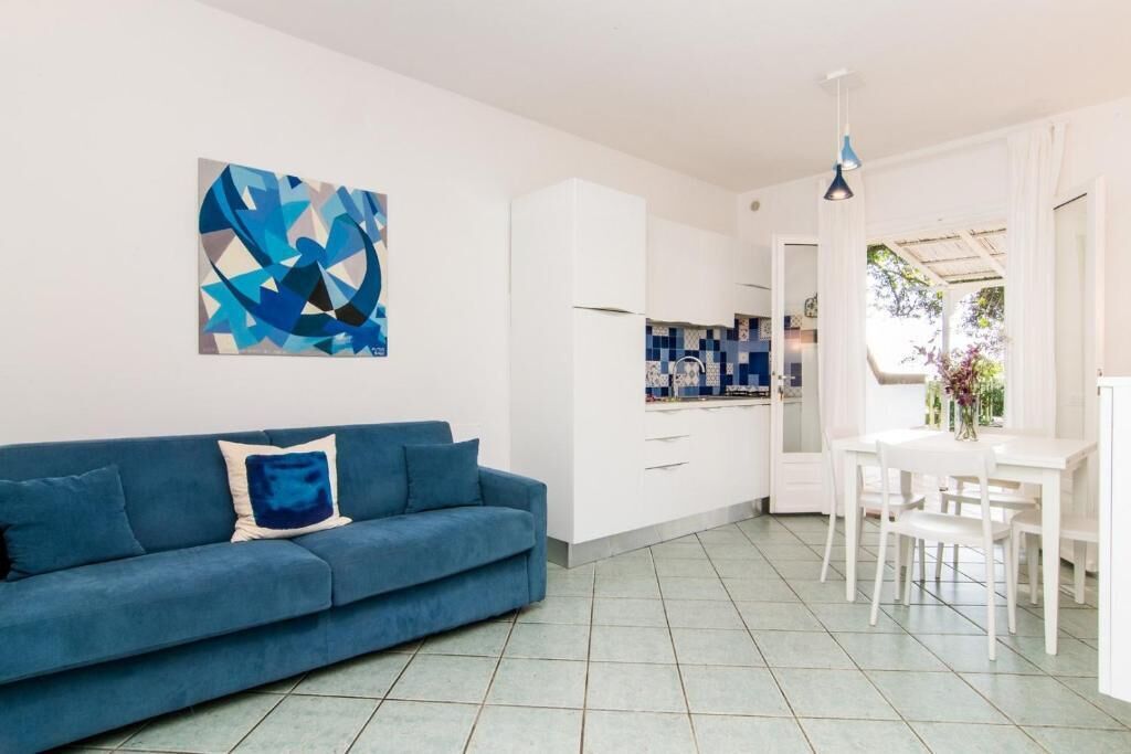 A modern living room with a blue sofa, white cabinets, and a dining area with a white table and chairs.