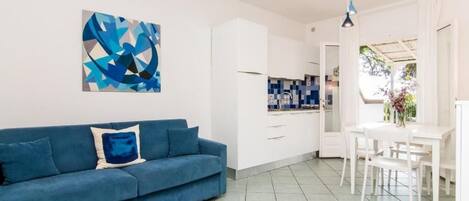 A modern living room with a blue sofa, white cabinets, and a dining area with a white table and chairs.