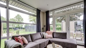 Ein modernes Wohnzimmer mit einer Eckcouch, einem runden Holztisch und großen Fenstern mit Blick ins Freie.