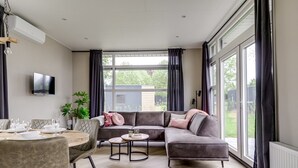 Ein modernes Wohnzimmer mit Ecksofa, Esstisch und großen Fenstern.
