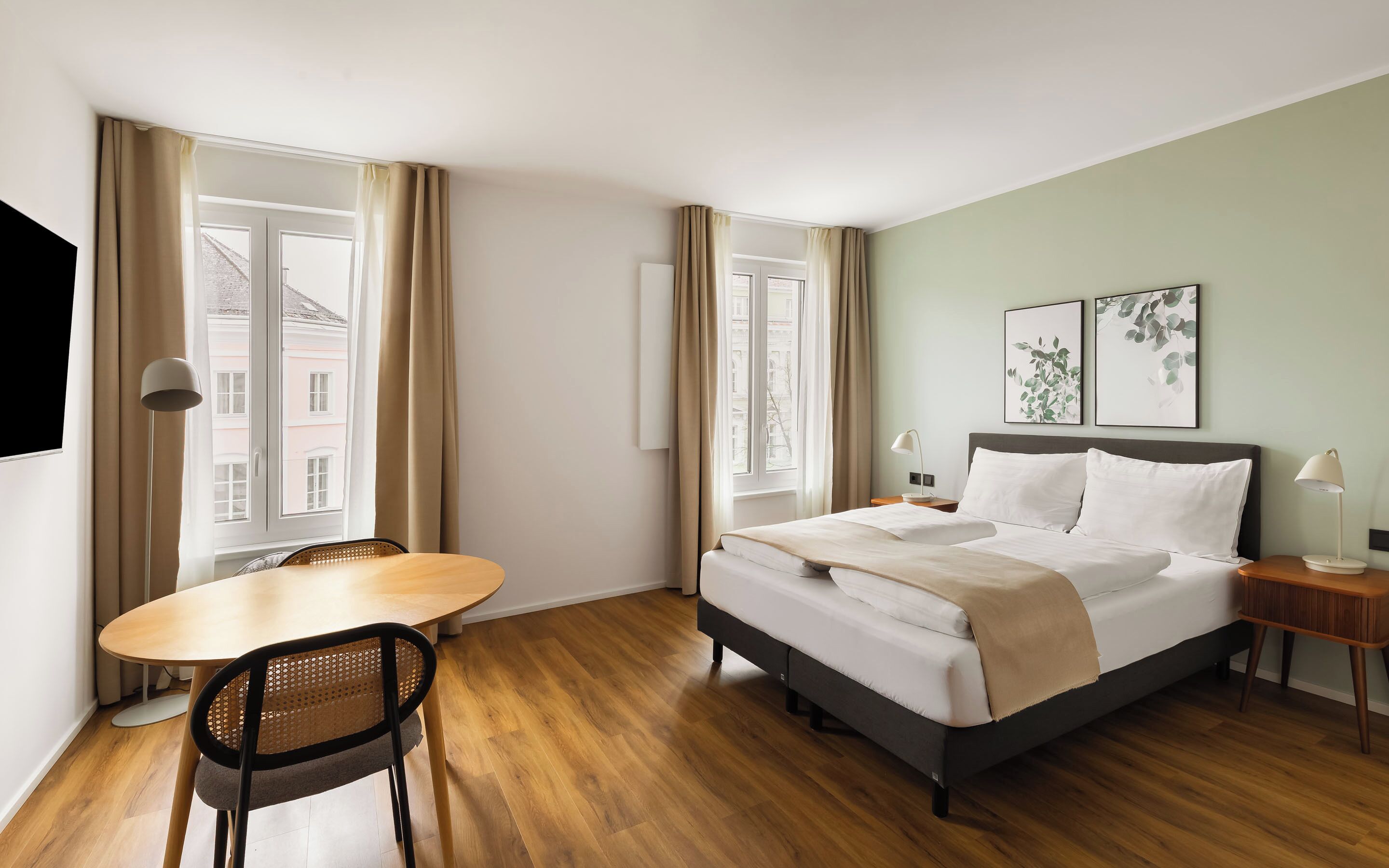 Ein Hotelzimmer mit einem Bett, Nachttischen, einem Sessel, einem Tisch und großen Fenstern mit Vorhängen.