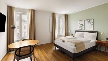 Ein Hotelzimmer mit einem Bett, Nachttischen, einem Sessel, einem Tisch und großen Fenstern mit Vorhängen.