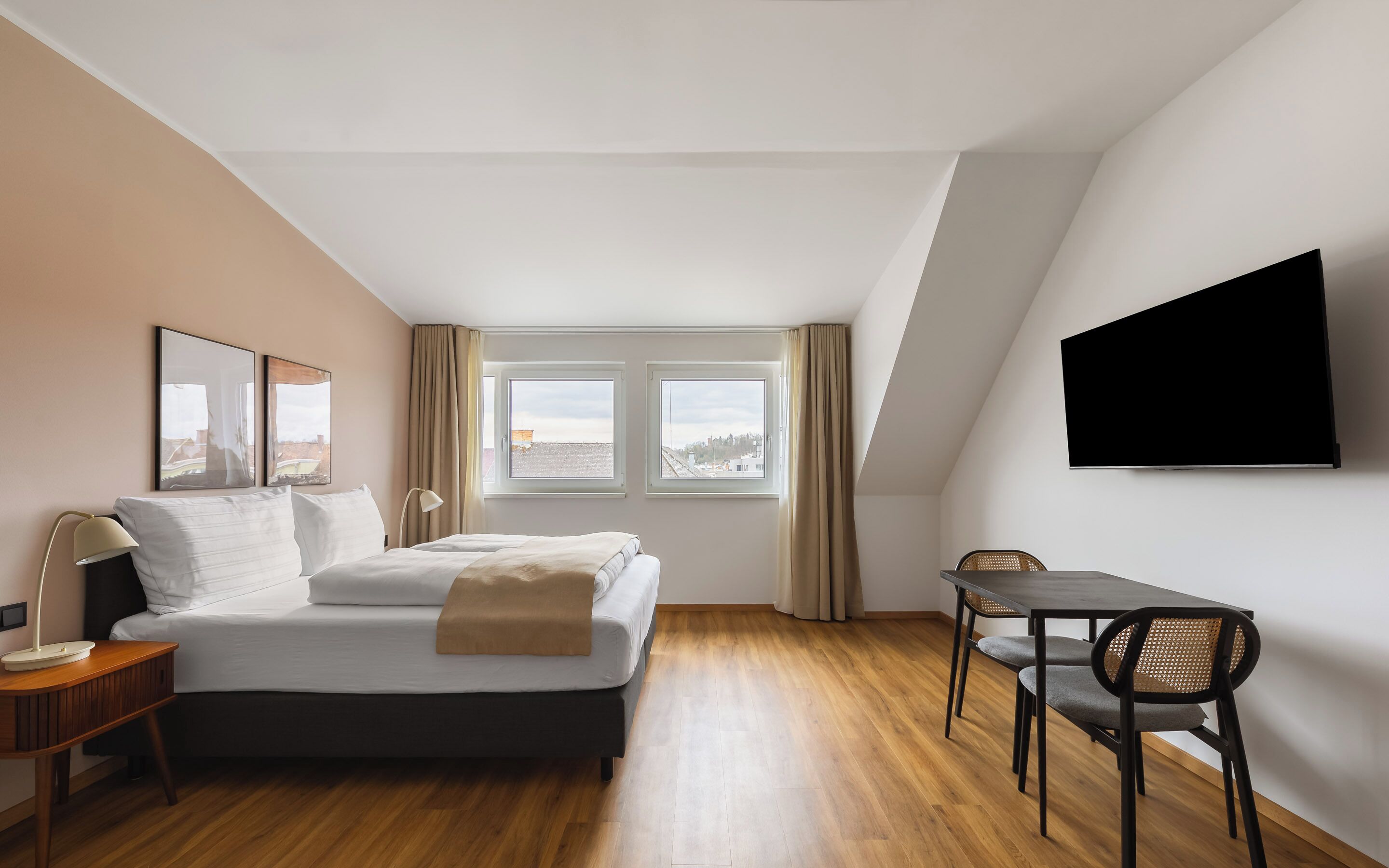 A modern hotel room with a bed, a desk, a chair, and a TV mounted on the wall.