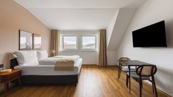 A modern hotel room with a bed, a desk, a chair, and a TV mounted on the wall.