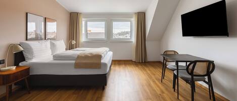 Una habitación de hotel moderna con una cama, un escritorio, una silla y un televisor fijado a la pared.