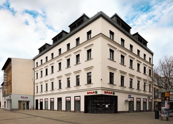Un immeuble à plusieurs étages doté d’une façade sobre, de plusieurs entrées au niveau du sol et d’une enseigne « SPAR » bien visible, indiquant la présence d’une épicerie.