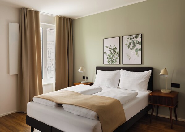 A neatly made bed with white and beige bedding, two bedside lamps, and two framed leaf artworks on the wall. - Limehome Wels Ringstraße (Wels)