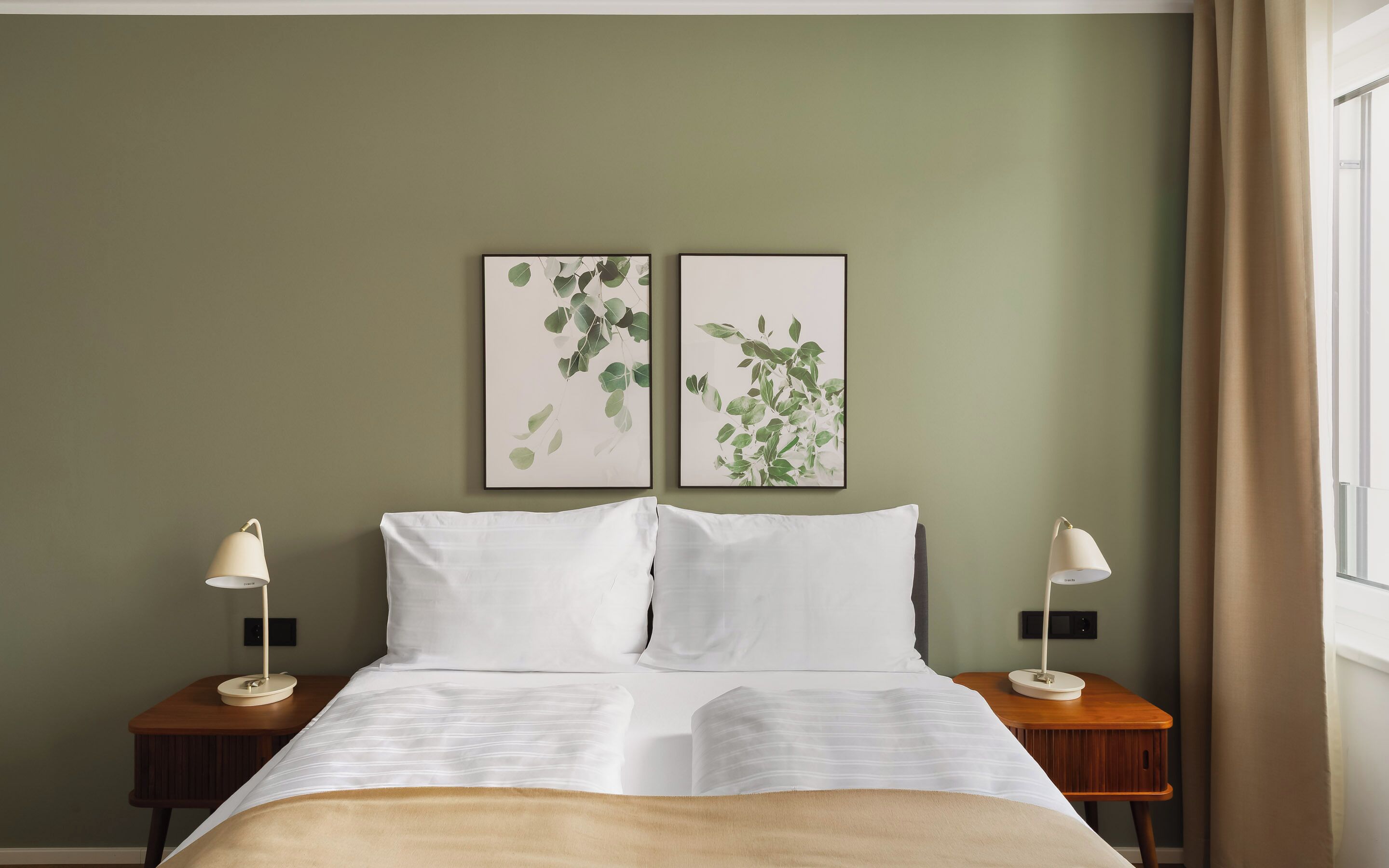 Ein Hotelzimmer mit einem Bett, zwei Nachttischen mit Lampen und zwei gerahmten Pflanzenbildern an der Wand.