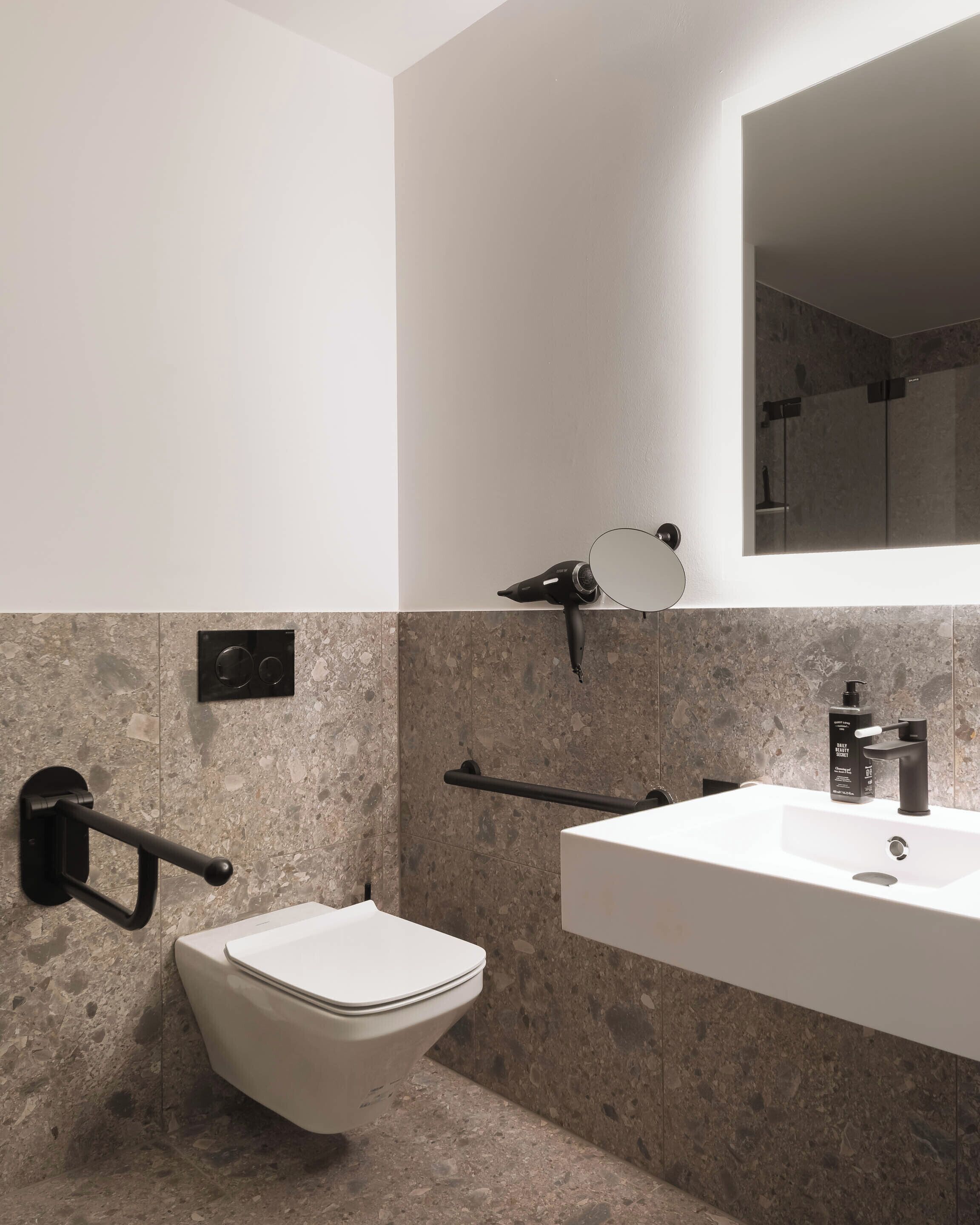 Un bagno moderno con il water bianco, un lavabo con rubinetto nero e uno specchio sopra il lavabo.