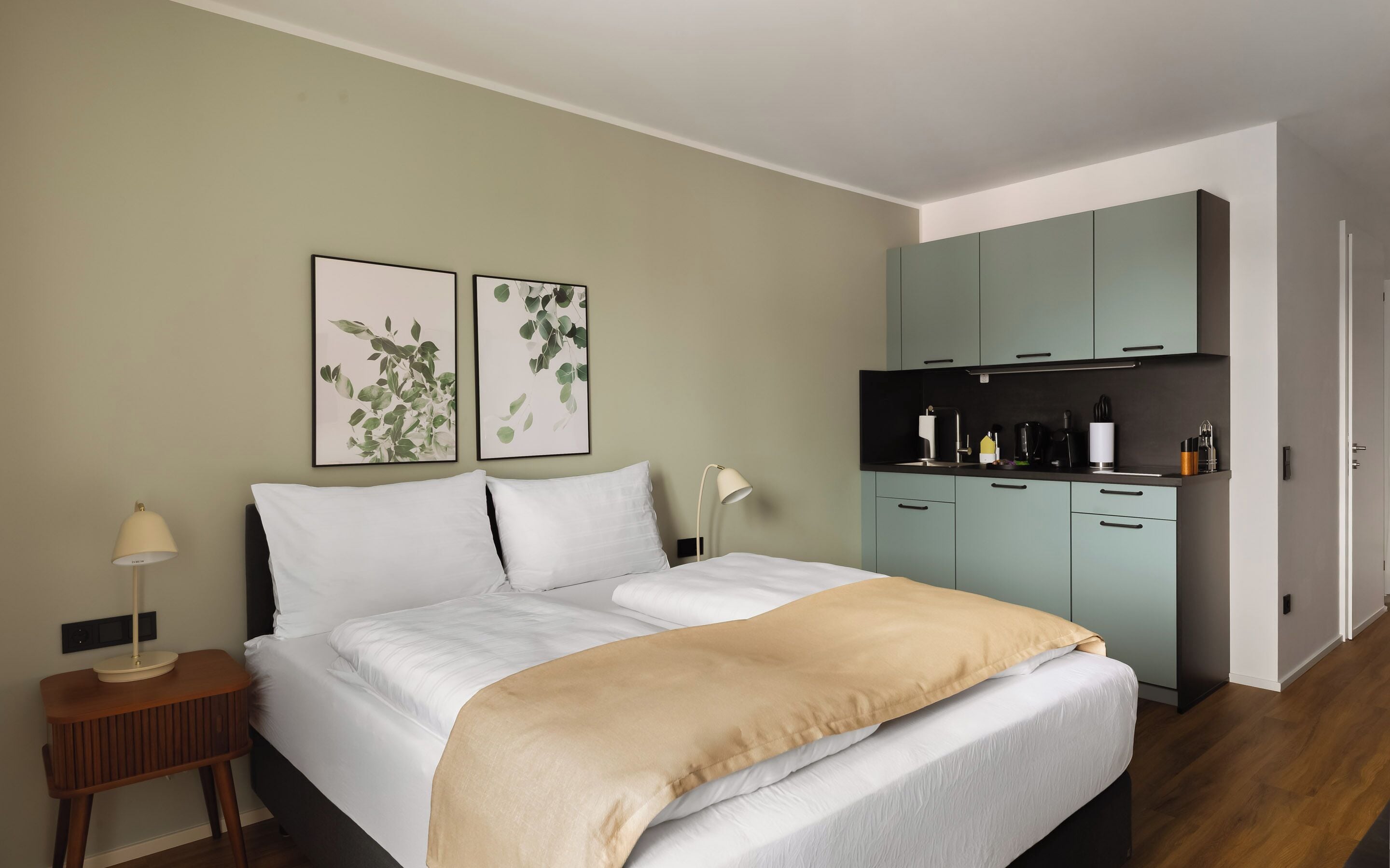 A bedroom with a bed, bedside tables, a lamp, a wardrobe, and two wall-mounted plant prints.