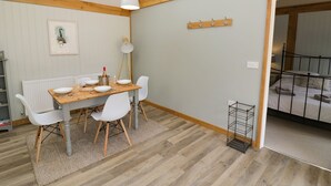 A dining area with a wooden table, white chairs, a radiator, and a framed picture on the wall. - Goose Lodge (Shipston on Stour)