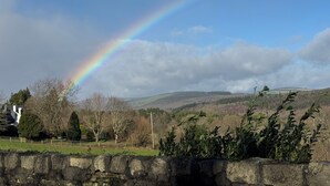 A stone wall, a rainbow, and a hilly landscape with trees.