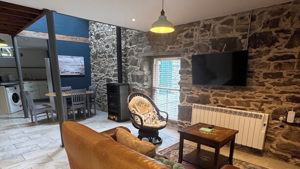 A living room with a sofa, a chair, a table, a television, and a stone wall.