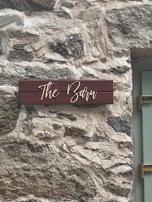 Une enseigne en bois portant l’inscription « The Barn » est fixée à un mur en pierre à la texture particulière.
