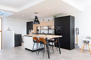 A modern kitchen with a central island, bar stools, and a high ceiling with recessed lighting.