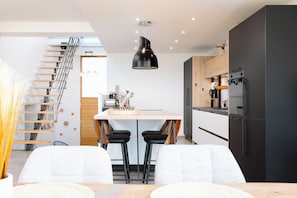 A modern kitchen with a central island, black pendant lighting, and a staircase.