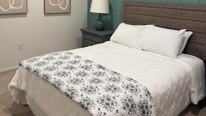A bedroom with a bed, a nightstand, a lamp, and two abstract wall art pieces.