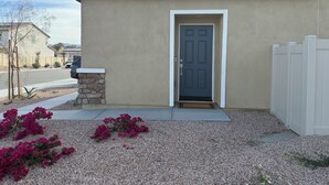 A residential building with a front door, a small stone planter, and a gravel driveway.
