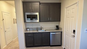 A kitchen with dark cabinets, a stainless steel microwave, a dishwasher, and a granite countertop.