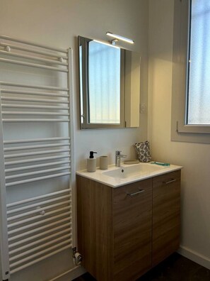 A bathroom with a white radiator, a mirror above a sink, and a window to the right. - 3-bedroom house, sleeps 8, Cordeliers (Parthenay)