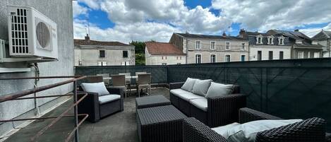 Une terrasse sur le toit, aménagée avec des meubles en osier, une rambarde en métal et offrant une vue sur les bâtiments environnants.