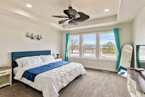 Une chambre à coucher avec un lit, un ventilateur de plafond, une fenêtre avec des rideaux et une table de chevet.