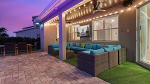 An outdoor patio with a sofa, chairs, and a TV screen.