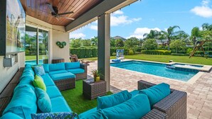 A covered outdoor area with a pool, wicker furniture, and a view of the surrounding landscape.