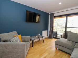 Ein modernes Wohnzimmer mit zwei grauen Sofas, einem Couchtisch und einem flachbildfernseher an der Wand.