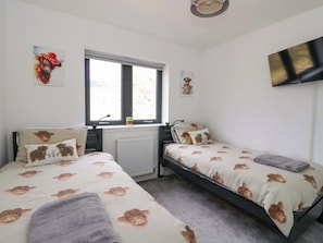 Ein Schlafzimmer mit zwei Betten, einem Fenster, einem Heizkörper und einem Fernseher an der Wand.