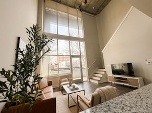 A modern living room with a large window, a sofa, a coffee table, a TV, and a staircase. - Boulevard Stays Midtown Nashville - BP (Nashville)