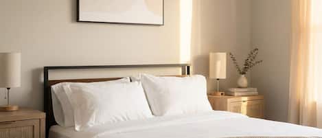 Una cama bien hecha con sábanas blancas, cabecera de madera y mesita de noche con lámpara.