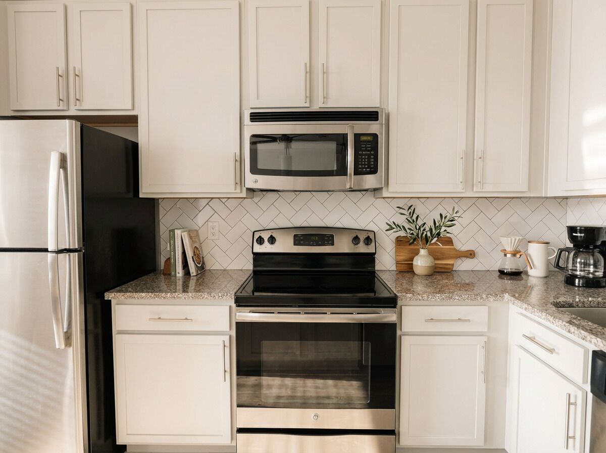 A kitchen with white cabinets, a stainless steel refrigerator, a microwave, an oven, and a coffee maker.