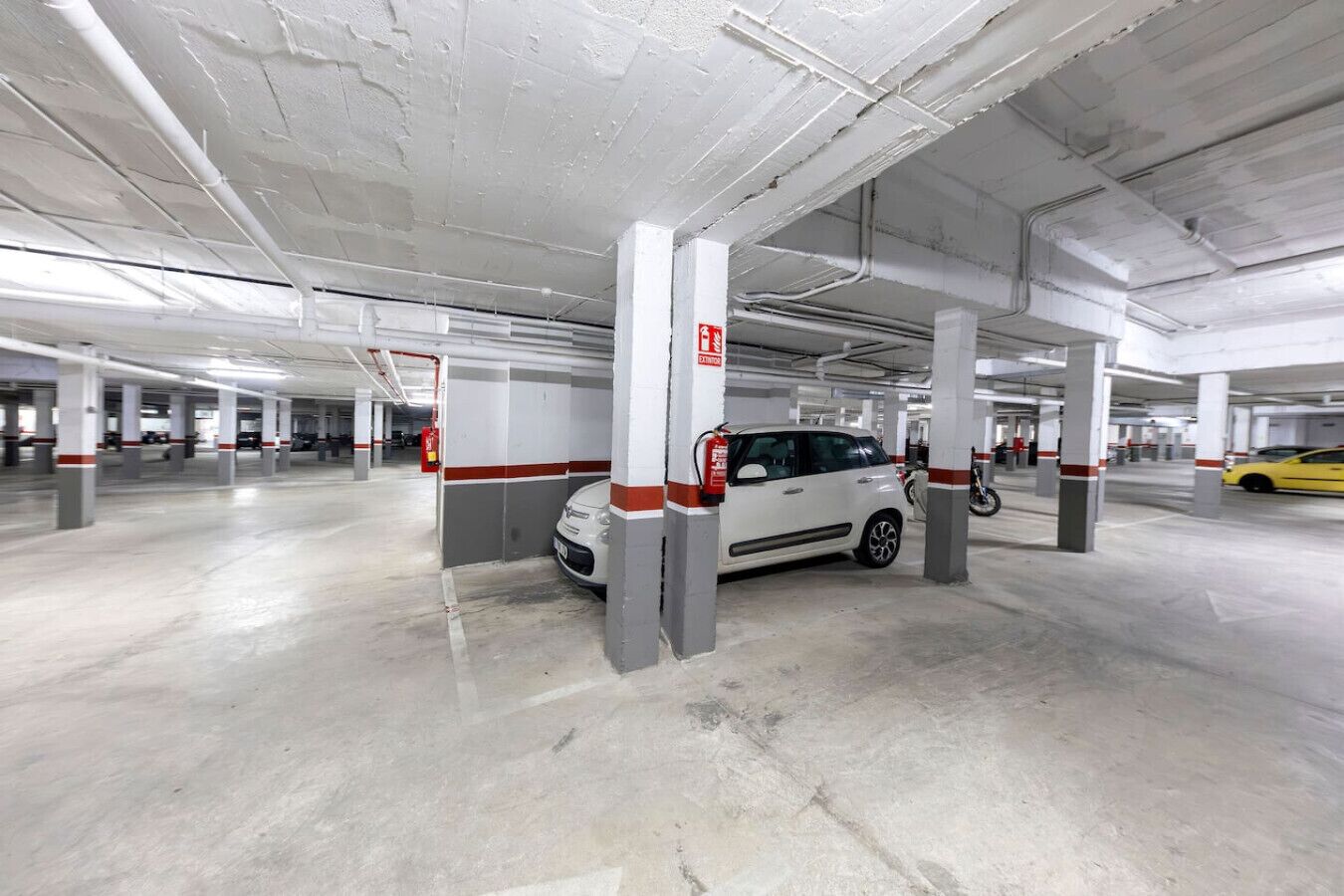 A multi-level parking garage with concrete pillars, clear signage, and a white car parked near a pillar.