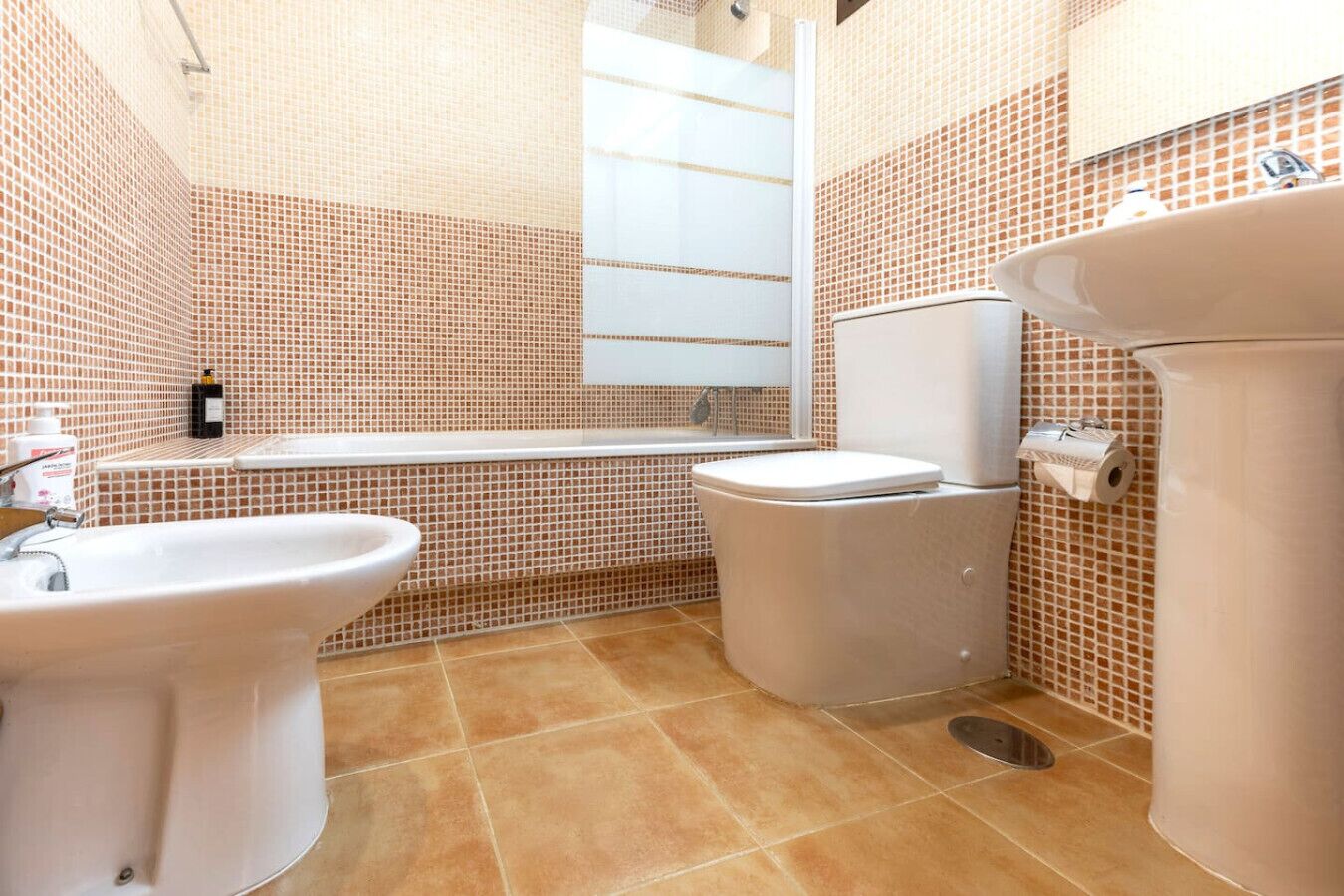 Un baño con bañera, inodoro y lavabo, con azulejos de diseño estampado.
