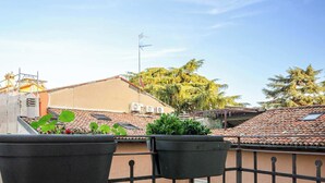 Ein Balkon mit Blumentöpfen, einem kleinen Tisch und Blick auf benachbarte Gebäude.