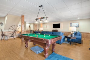 Ein Billardtisch in einem Raum mit Holzboden, einem blauen Sofa und einem an der Wand befestigten Fernseher.