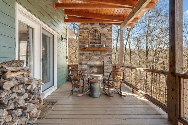 Eine Holzterrasse mit Kamin aus Stein, Korbstühlen und einem Metallfass.